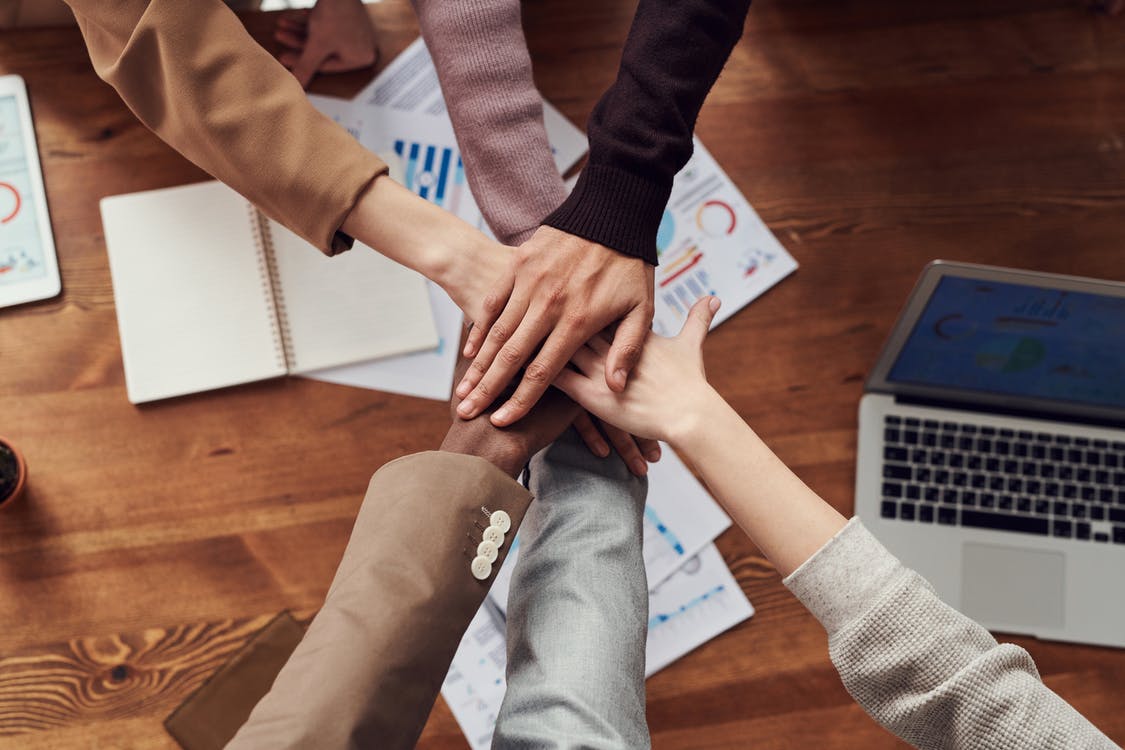 The hands of a team, meeting over a desk with paper and a laptop computer